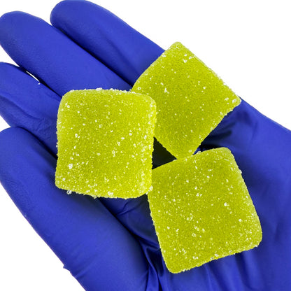 Tas de gummies au THC verts goûts pomme sur fond blanc tenu dans une main